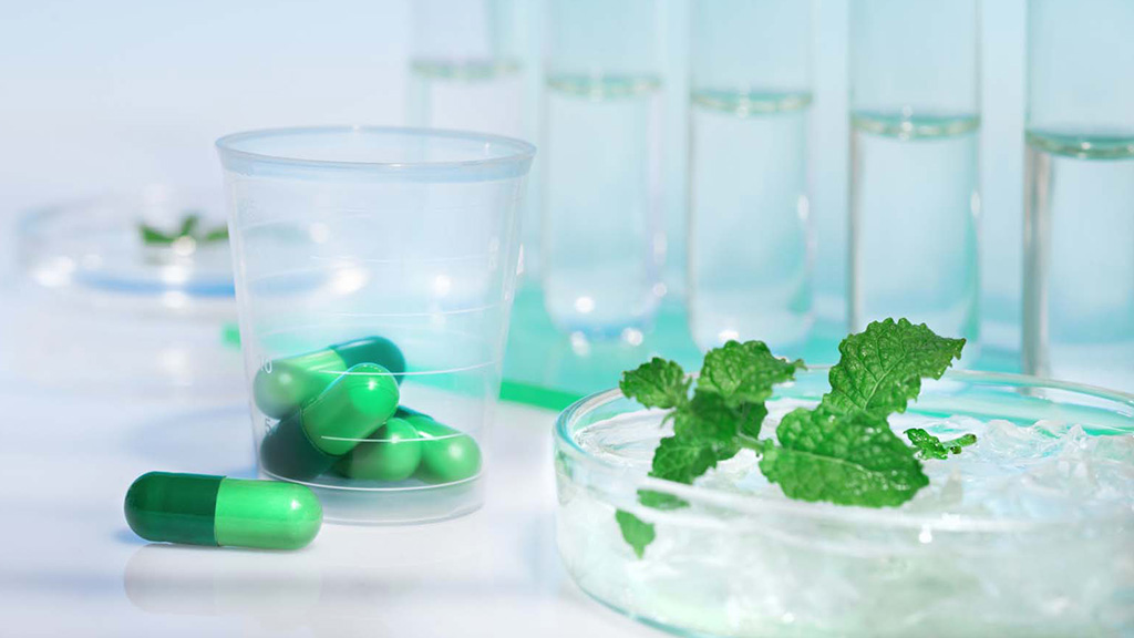 Green pills in a plastic cup, and two mint leaves in a bowl