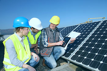 Three men kneeling next to a solar panel.