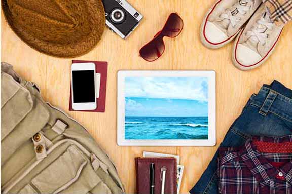 Decorative image of Summer materials. Included is a tablet device, phone, sunglasses, camera, hat, shoes, pants, shirt and backpack.