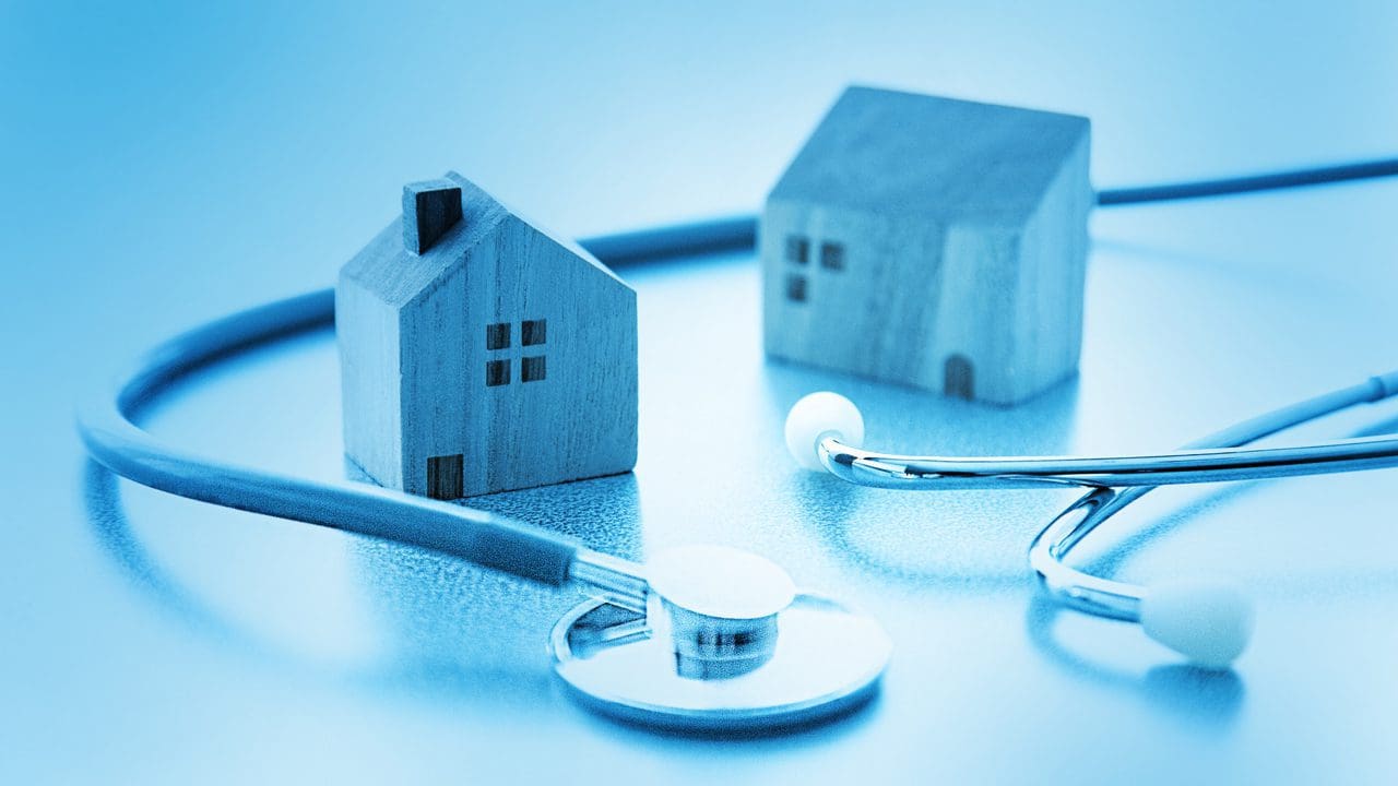 Image of a stethoscope wrapped around two paper houses.