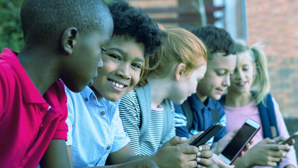Five seated children smiling and looking at smartphones