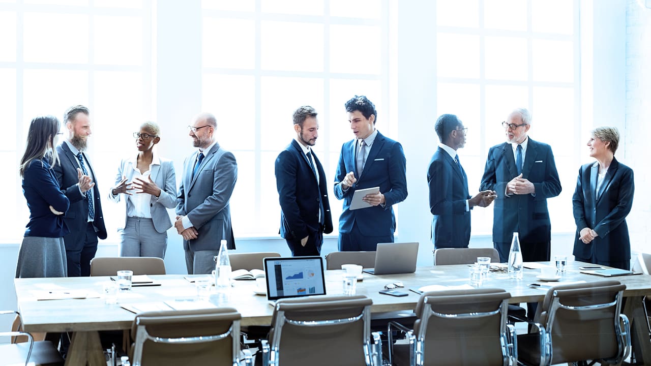 Stock photo of several people talking while standing in a meeting room.