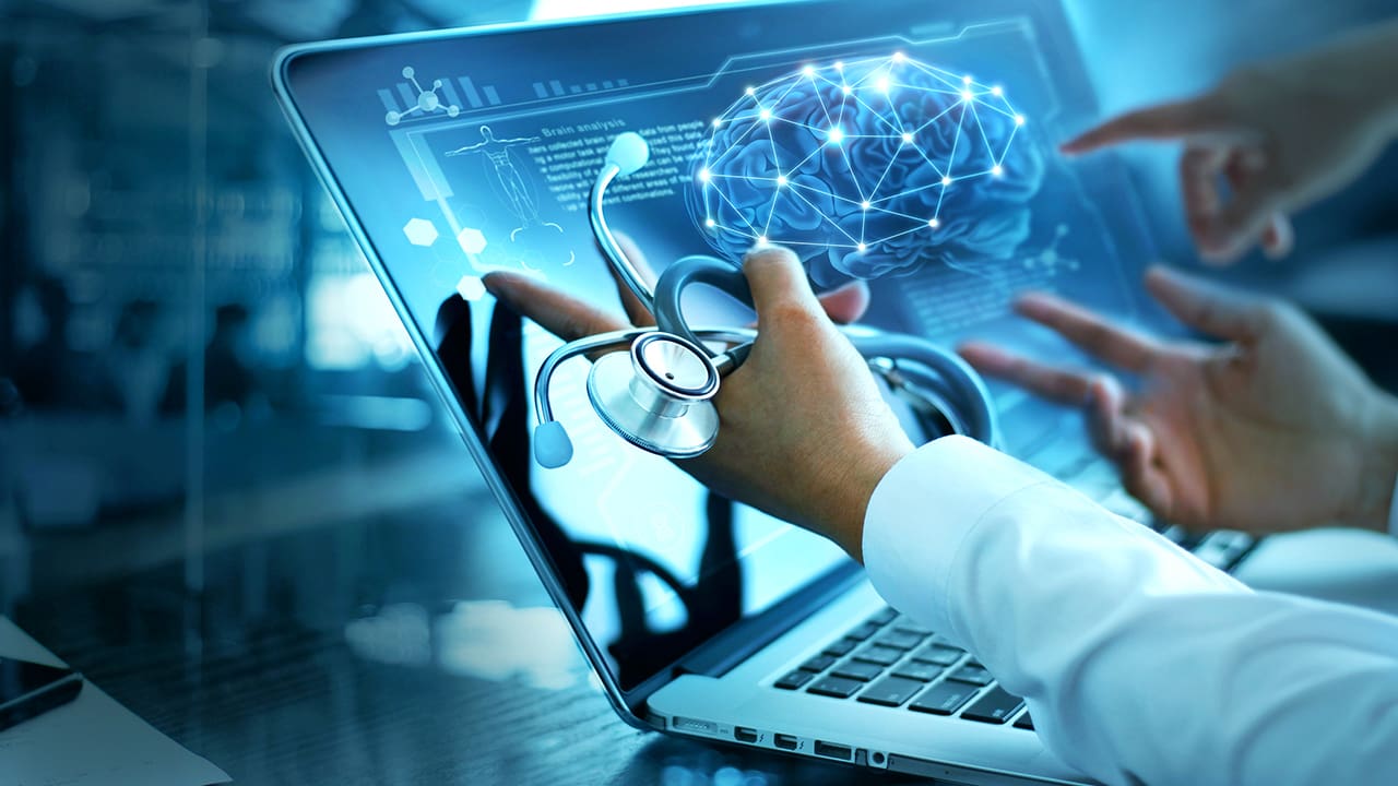 Doctor holding a stethoscope while pointing to a laptop with an image of a brain on it.